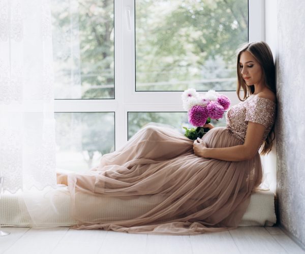 Sensetive portrait of pregnant woman. Expecting lady lies on the windowsill in a bright room