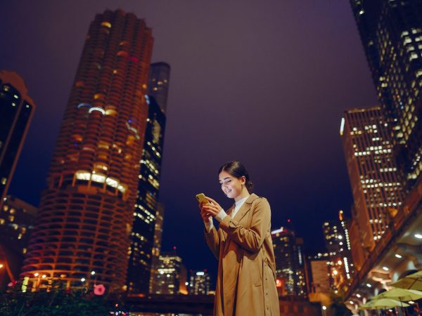 young brunette girl standing at night with phone by Chicago skyline