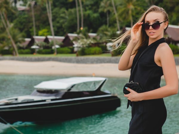 luxury sexy attractive woman dressed in romantic black dress posing on pier in luxury resort hotel, wearing sunglasses, summer vacation, tropical beach