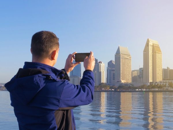 Young male tourist makes photos from his travels for placement in social networks. Social networks are a modern trend. Looks at the mobile phone screen after shooting a photo. Photos from the trip.